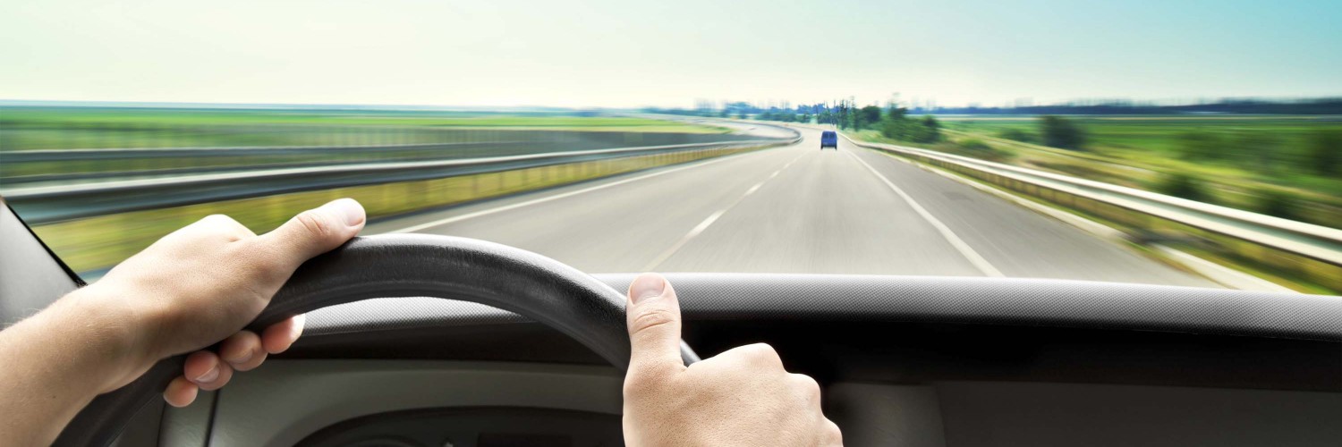 Man's hands of a driver on steering wheel of a minivan car on asphalt road